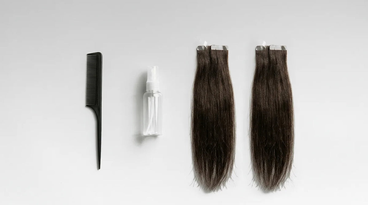 Peigne à queue, flacon pulvérisateur sans étiquette et deux mèches d'extensions adhésives brunes sur fond gris