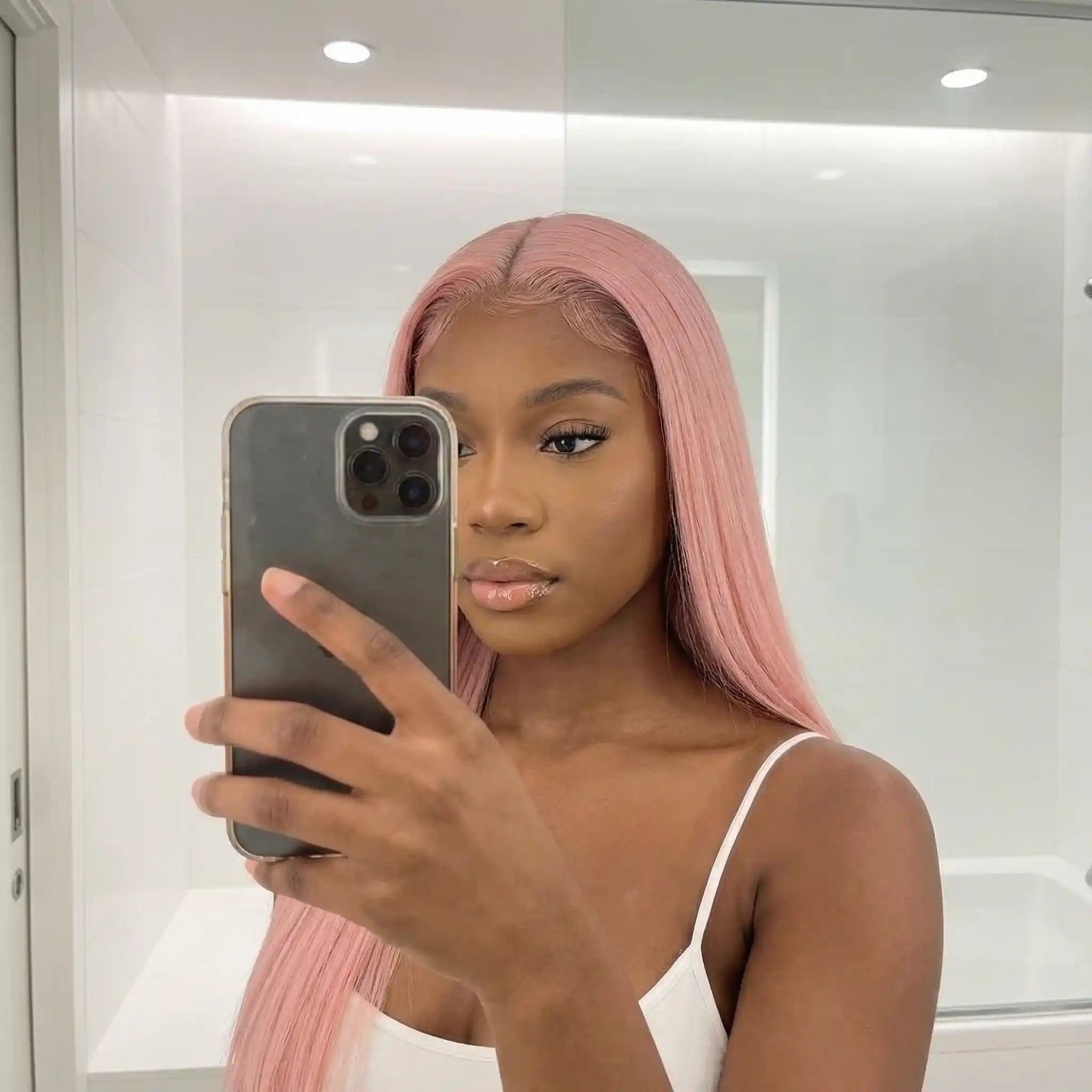 Femme portant une perruque rose pastel longue avec lace invisible et baby hair naturels, selfie miroir lumineux.