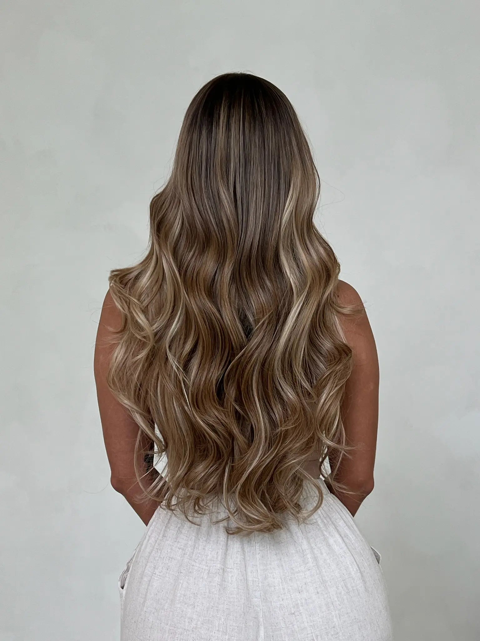 Femme de dos portant un projet personnalisé Carthair avec extensions adhésives Virgin Hair 12A couleur miel caramel, au rendu naturel et soyeux.